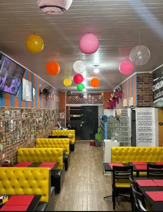 Ambiente real da Chiquinha, com bancos amarelos, mesas escuras e decoração colorida